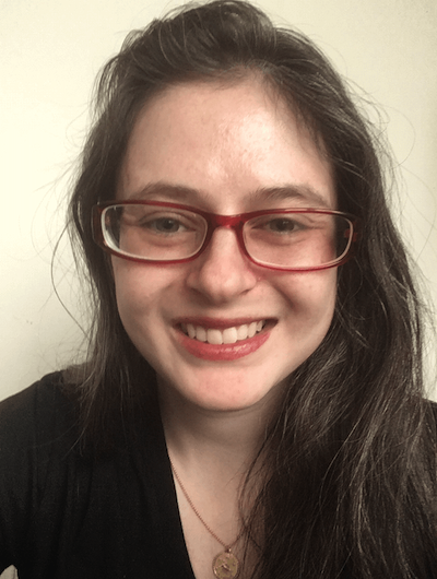 Ryn Silverstein, a white person with dark hair and red glasses, smiles at the camera